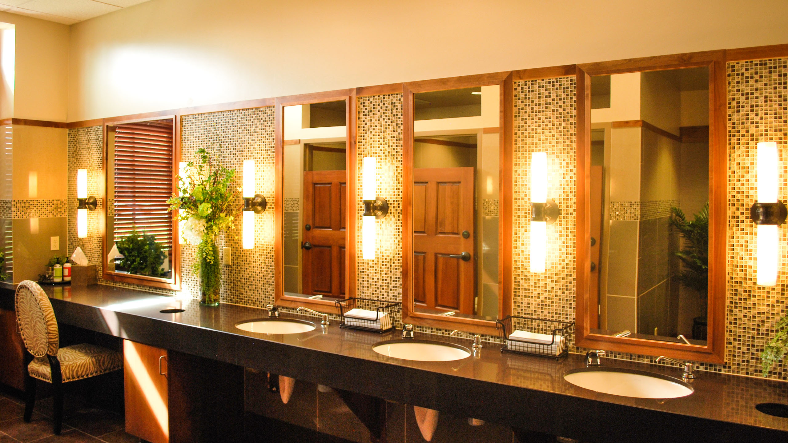 Elegant restroom at the Priest River Event Center in Idaho, featuring a long vanity with multiple sinks, wood-framed mirrors, mosaic tile backsplash, soft vertical lighting, and decorative floral arrangements.