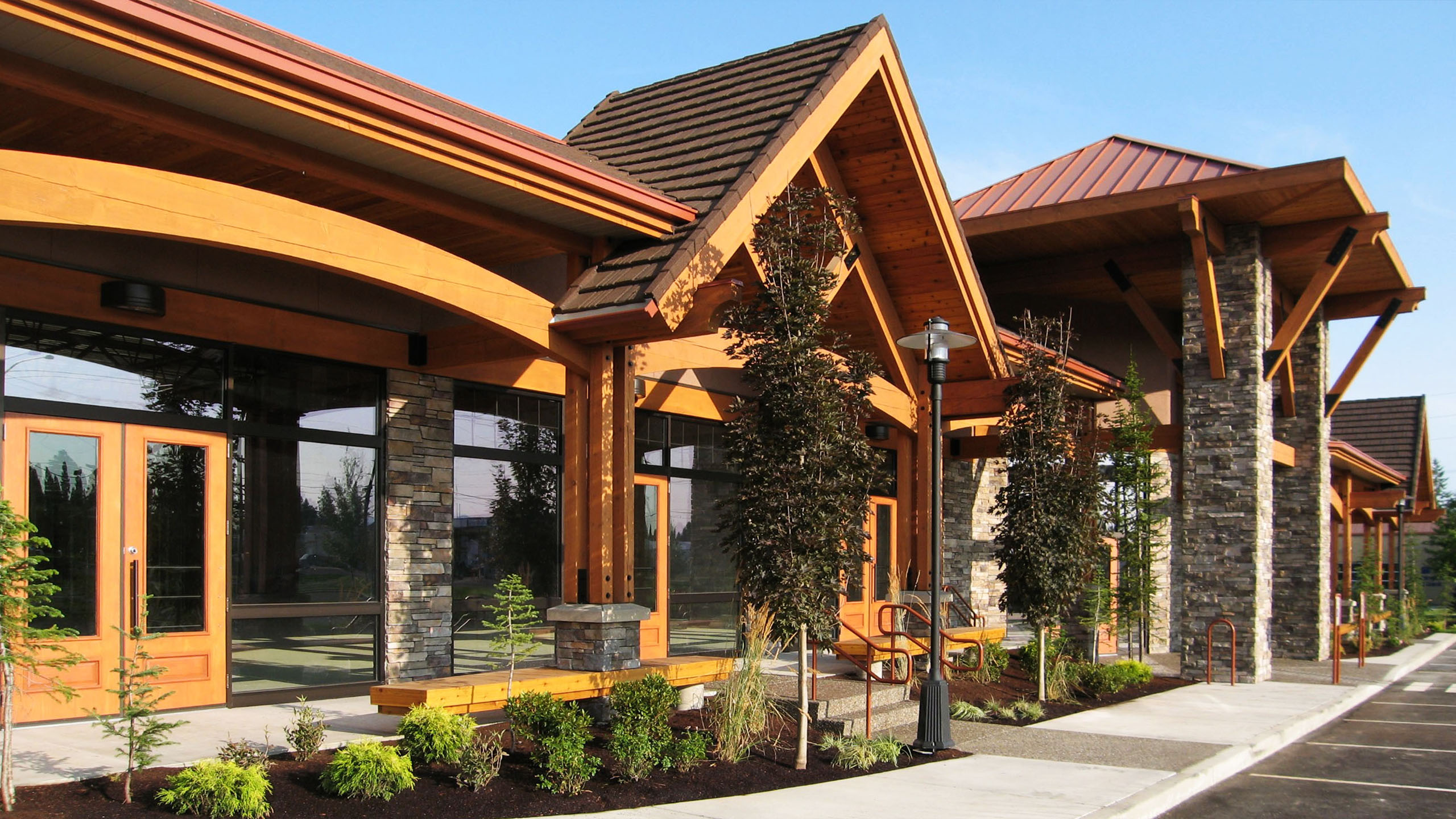 Front view of Hayden Creek Plaza in Hayden, Idaho, featuring timber-framed retail storefronts, stone columns, and landscaped walkways.