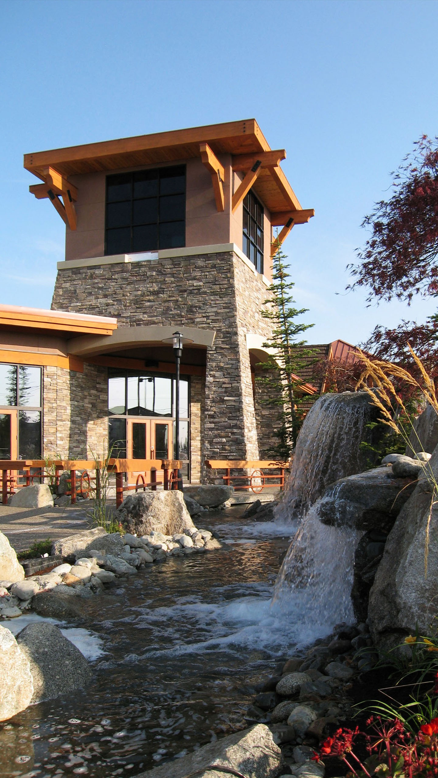 Stone tower and waterfall feature at Hayden Creek Plaza in Hayden, Idaho, with landscaped stream and wooden architectural accents.
