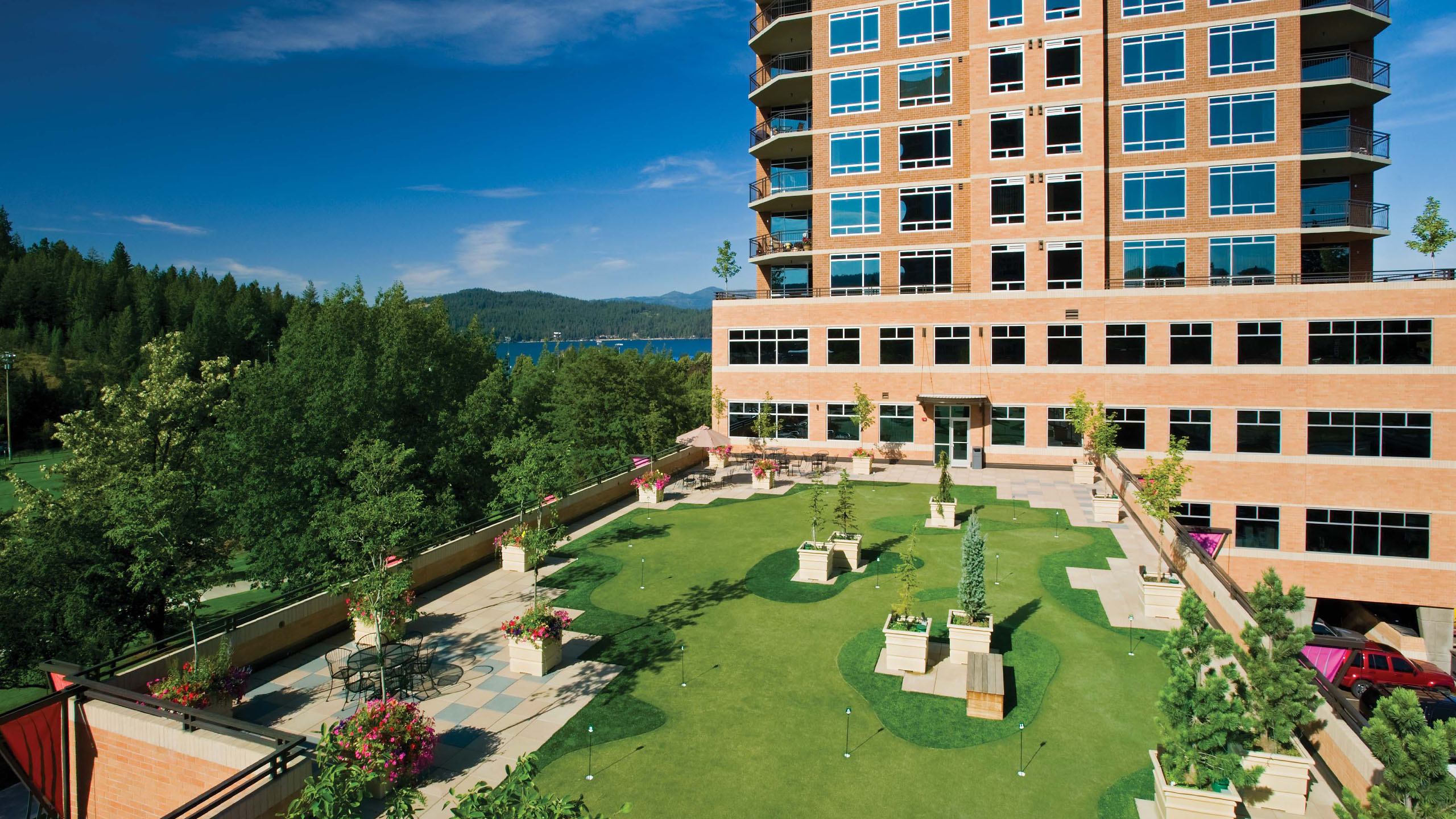 View of Parkside’s rooftop putting green and terrace in Coeur d’Alene, Idaho, featuring landscaped planters, seating areas, and scenic views of Lake Coeur d’Alene and surrounding pine-covered hills in the background.
