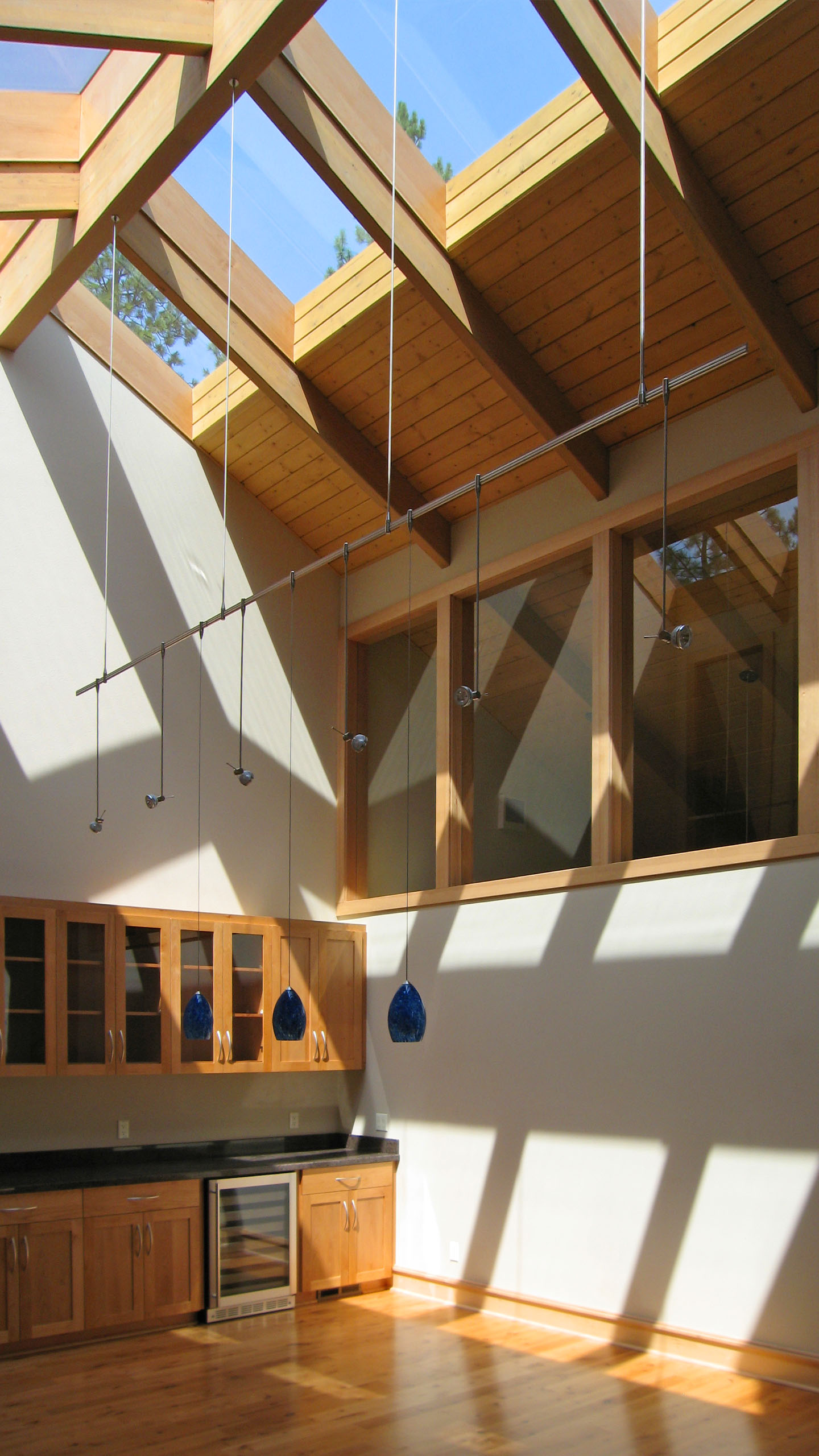 Interior view of a kitchenette at Spokane River Residence, featuring wood cabinetry, a mini fridge, and dramatic natural light streaming through skylights and exposed timber beams.