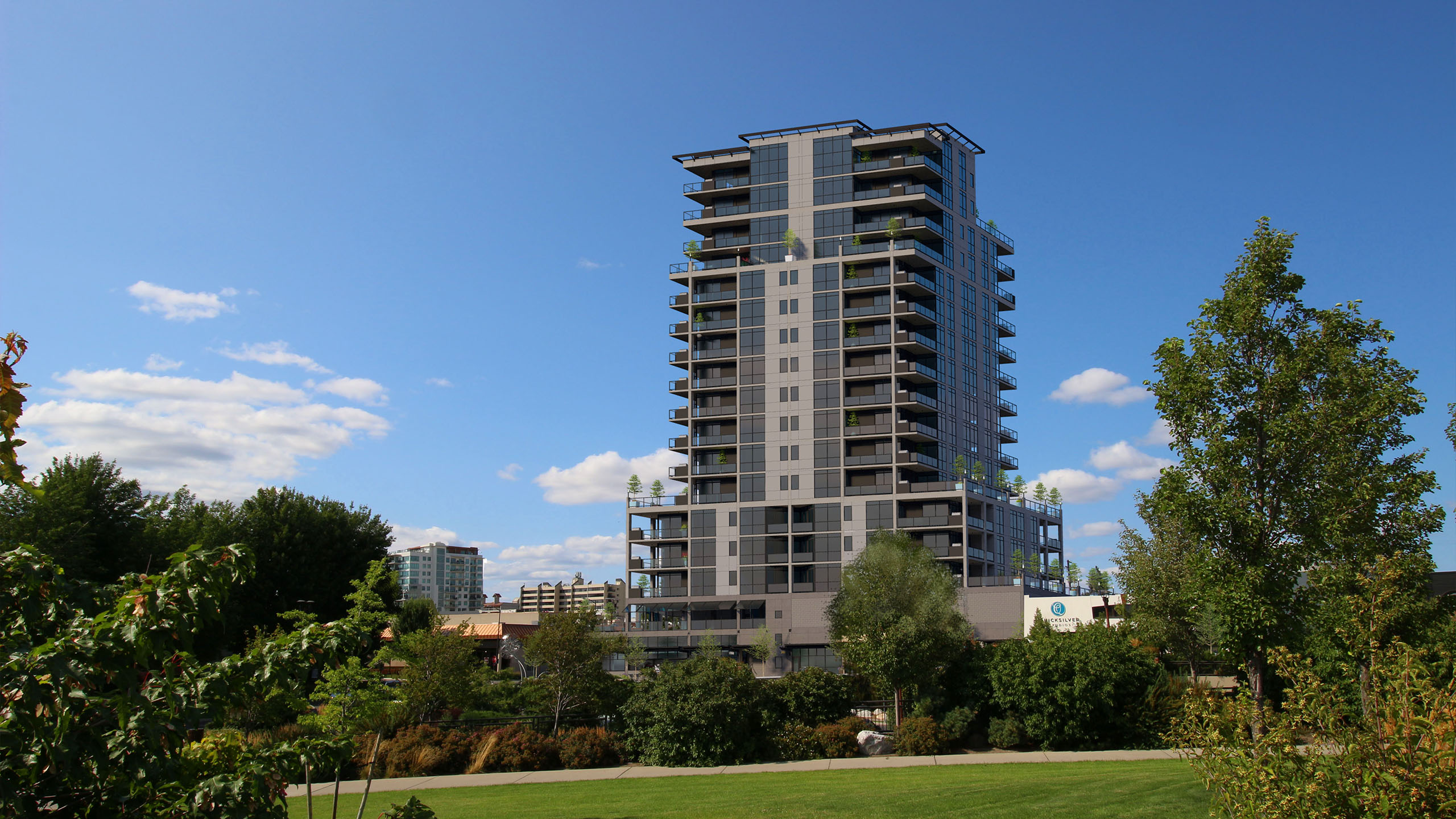 Daytime view of The Thomas George condominium tower in Coeur d’Alene, Idaho, with adjacent green space and landscaped foreground.