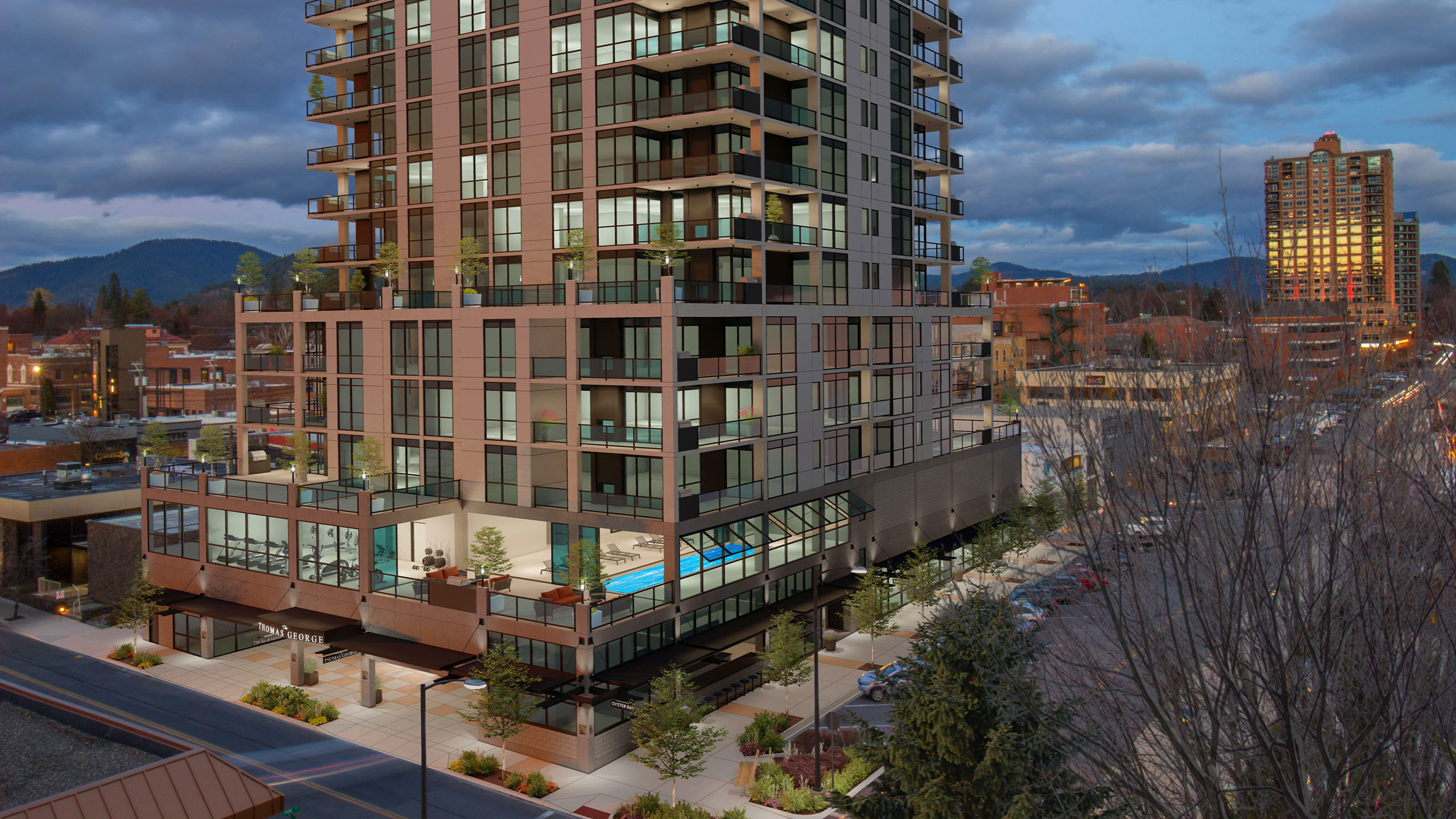 Evening exterior of The Thomas George in downtown Coeur d’Alene, featuring floor-to-ceiling windows, private balconies, and illuminated amenity spaces.
